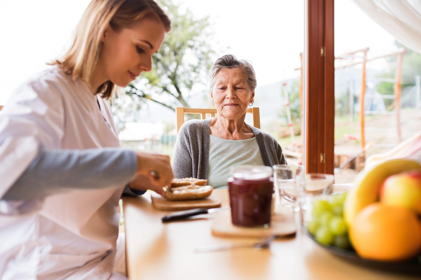 A caregiver and an older woman sharing breakfast together at a sunlit kitchen table